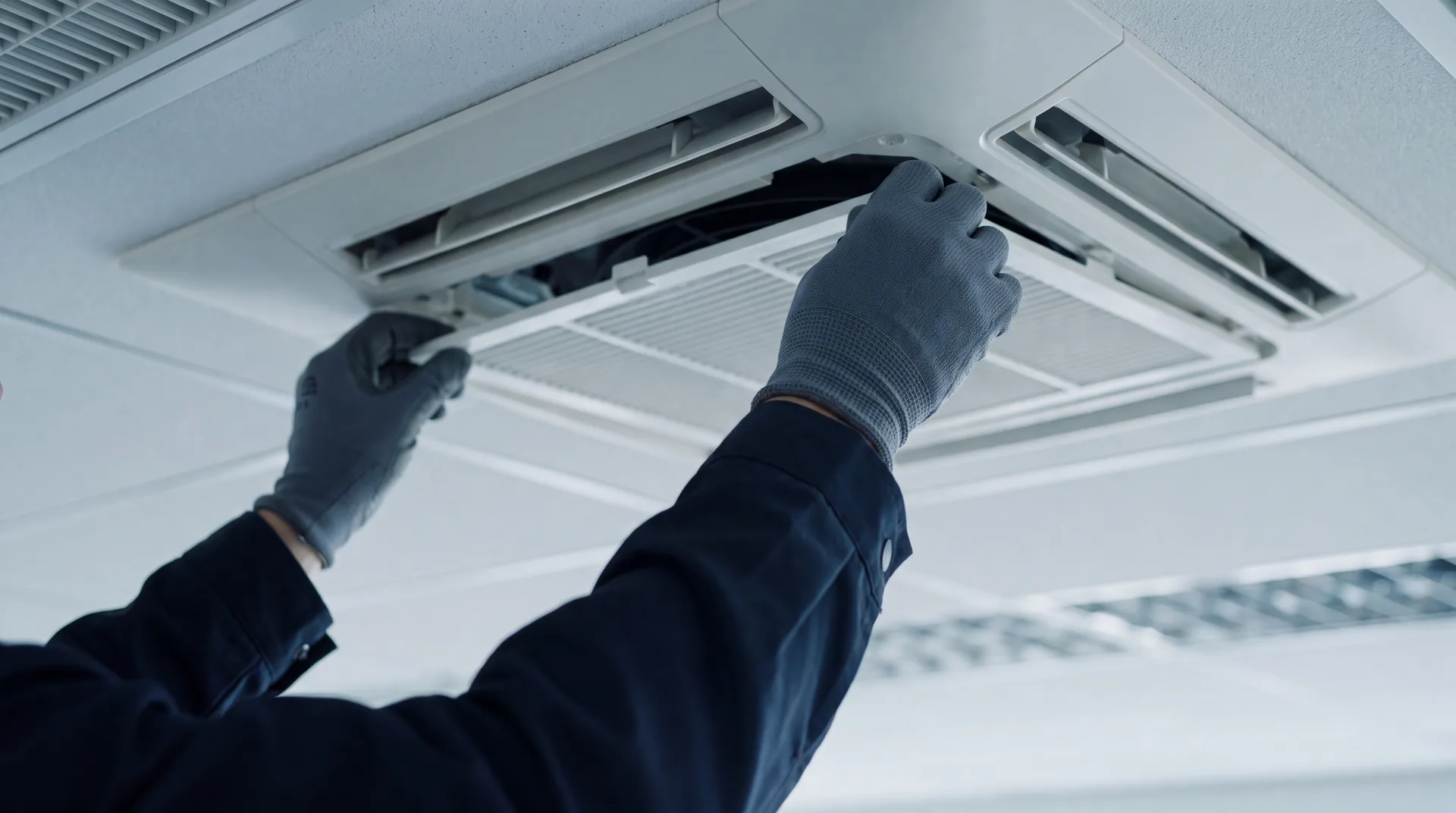Mains gantées d'un technicien retirant le filtre d'une cassette de plafond lors d'une visite d'entretien.